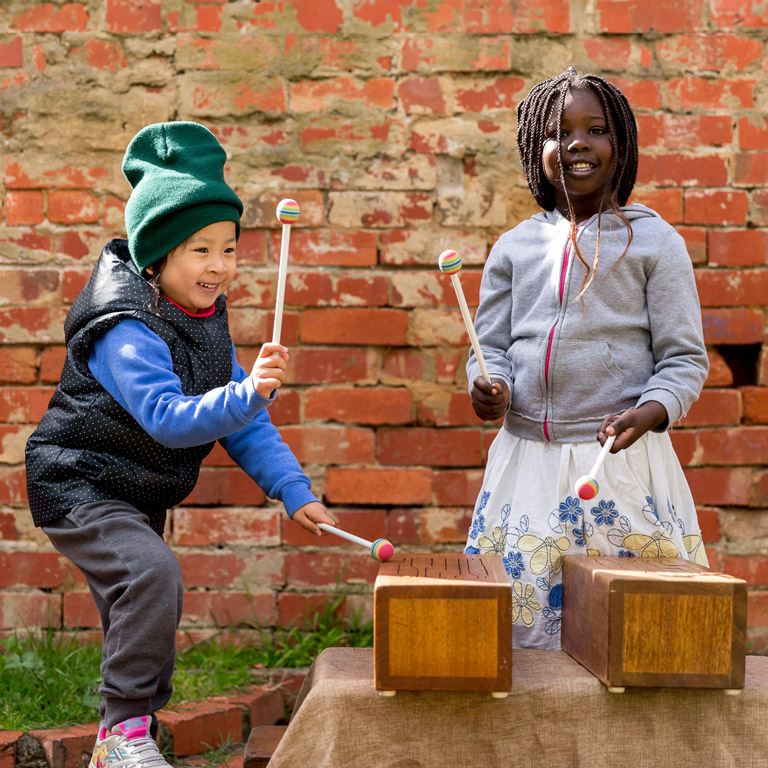 Two children playing outside with drums